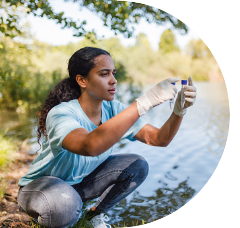 Young person crouching down near shoreline holding two test tubes with water samples