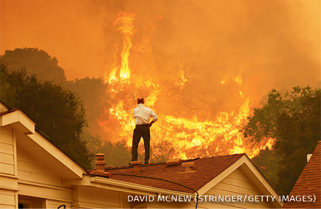 An image of a man on a rooftop looking at approaching flames.