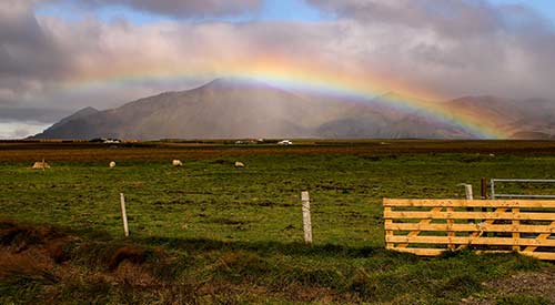 Fence in the foreground with rainbow over mountains in the background